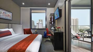 Habitación de hotel moderna con una cama grande, un escritorio, una silla, un televisor y un balcón con vistas a la ciudad.