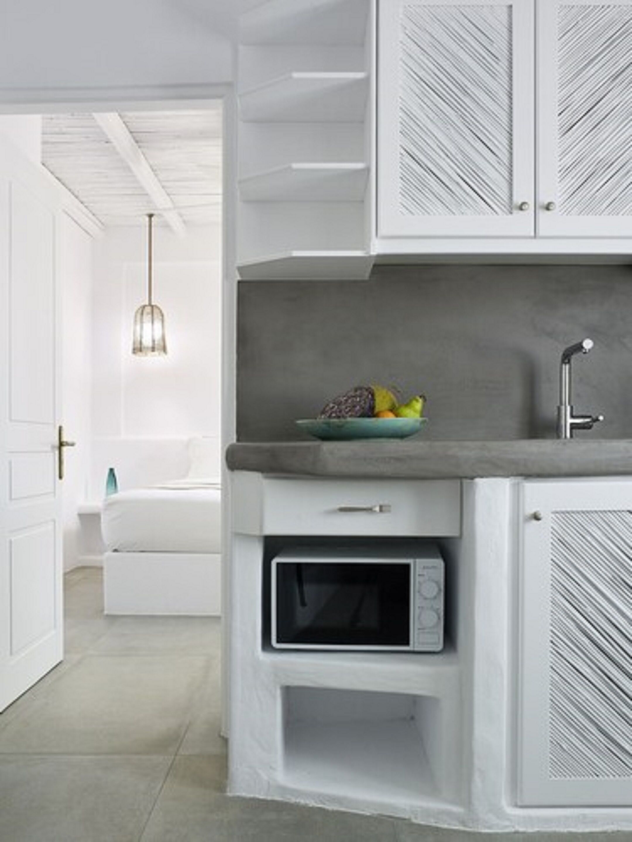 A modern kitchen with white cabinetry, a built-in microwave, and a fruit bowl on the countertop.
