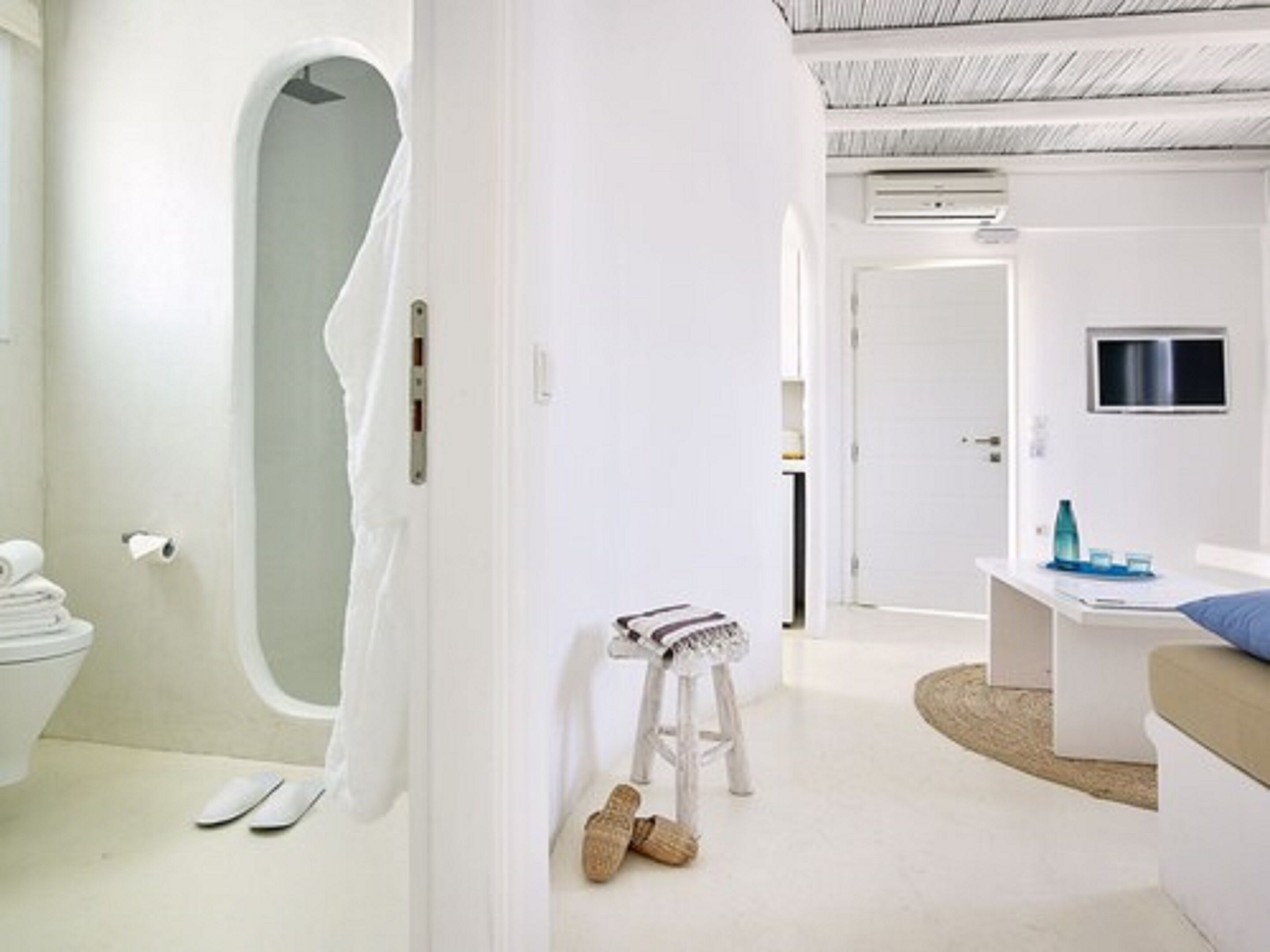 A modern bathroom with a bathtub, toilet, and shower. There is a small stool with a towel and slippers.