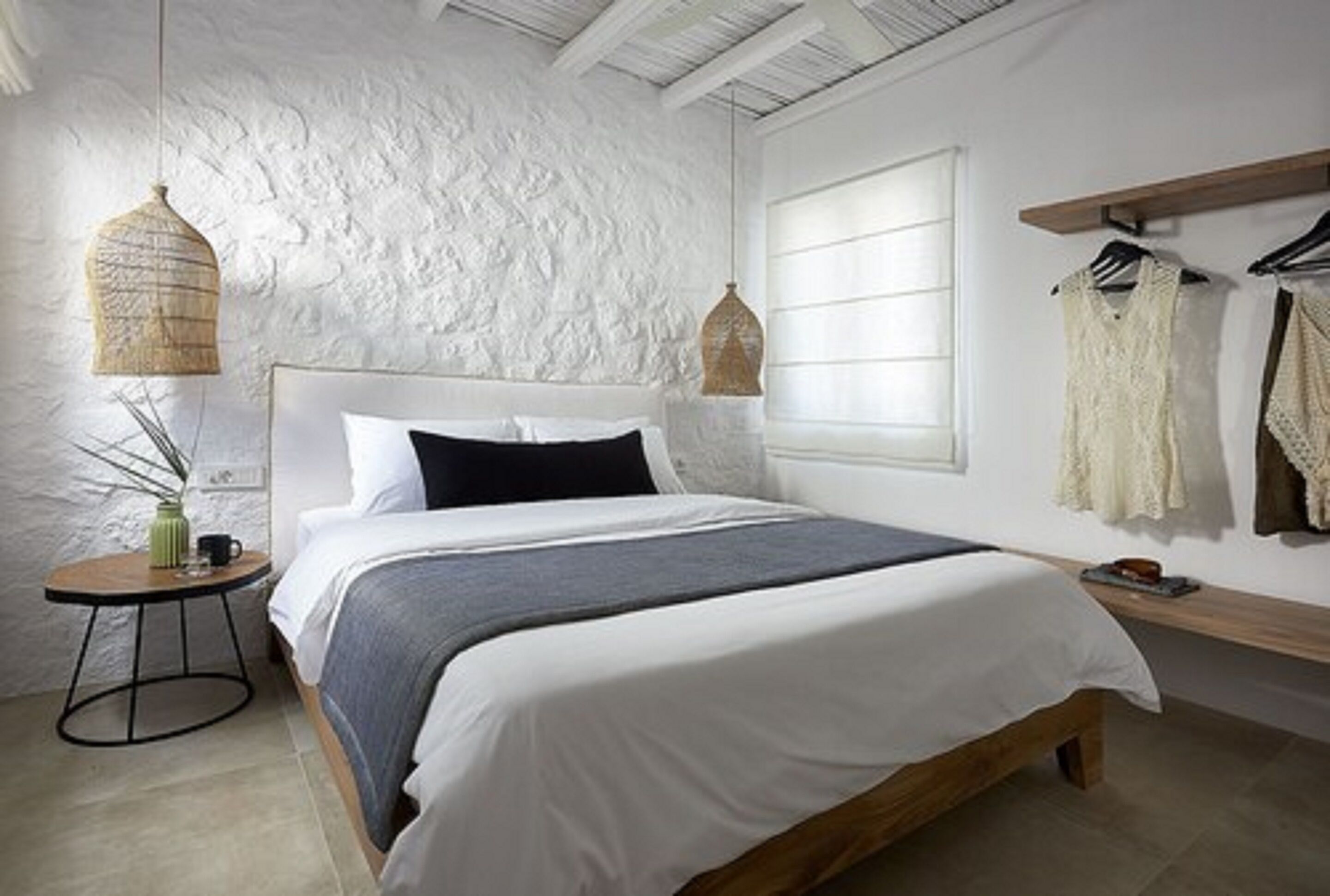 A bedroom with a white textured wall, a bed with a wooden frame, a round side table, and two hanging light fixtures.