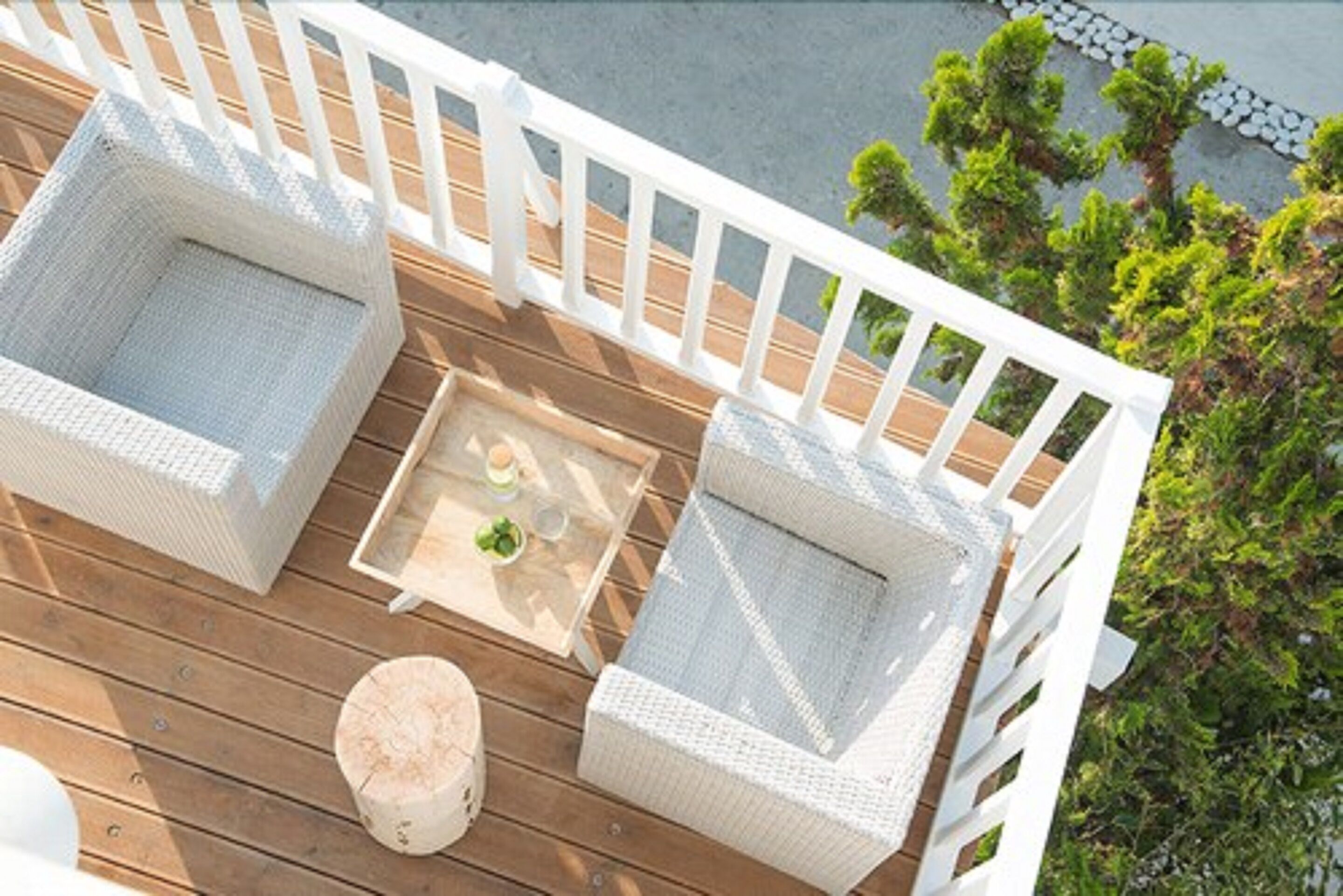 A wooden deck with two wicker chairs and a small table, surrounded by a white railing.
