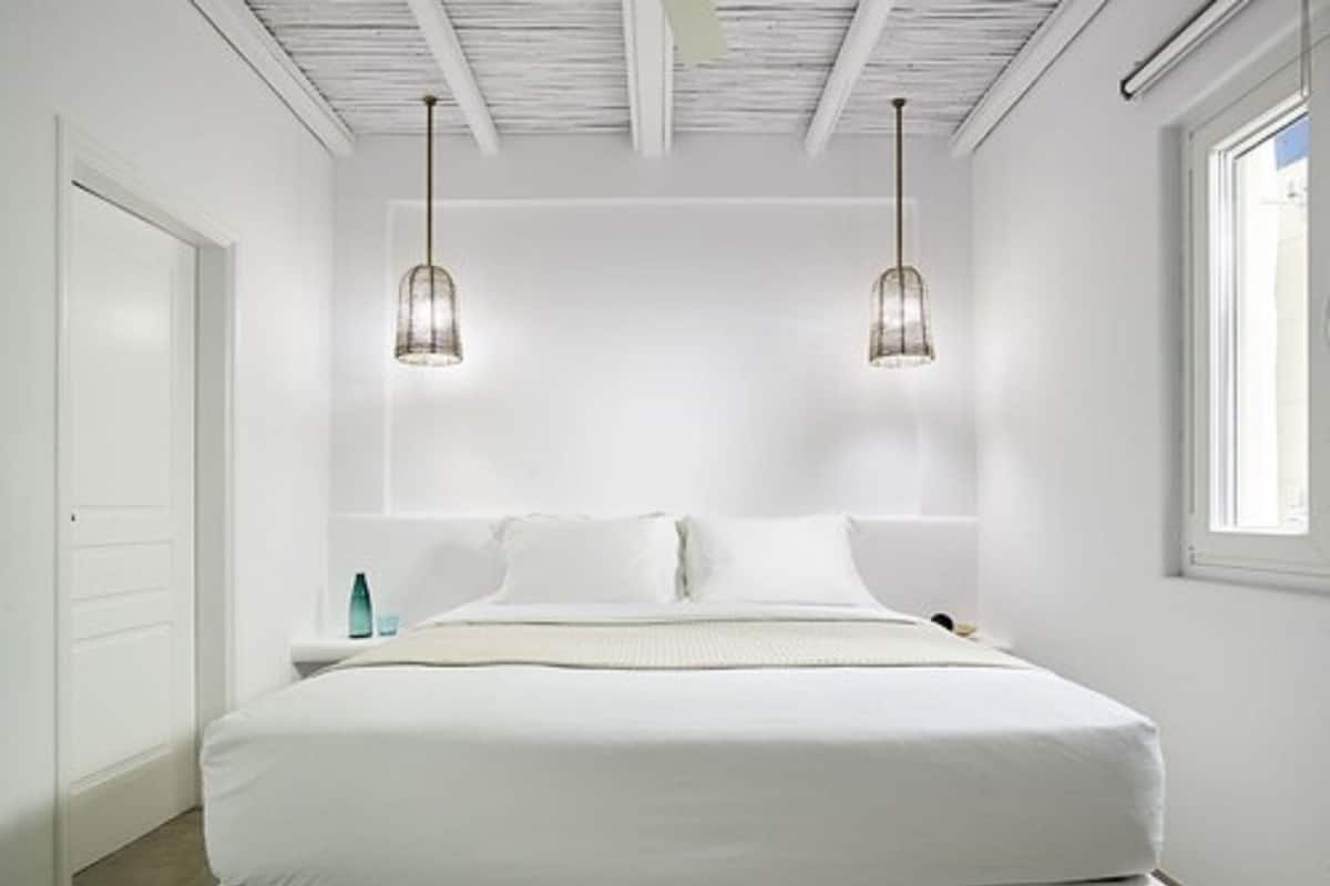 A modern bedroom with a large bed, two pendant lights, a nightstand, and a window.