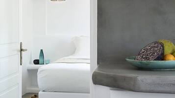 Un dormitorio con una cama, una mesita de noche con una lámpara y un frutero sobre un tocador.