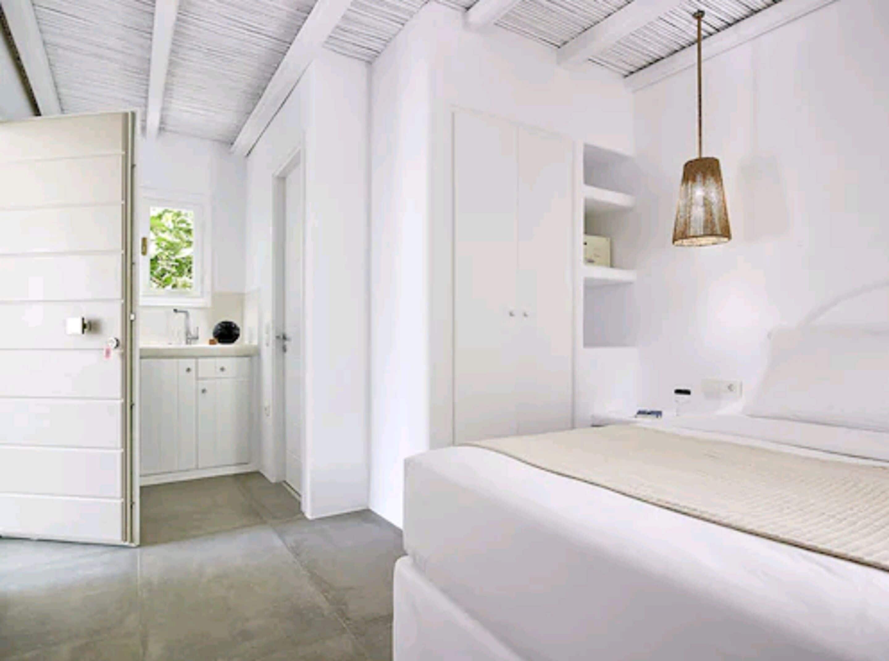 A modern bedroom with a large bed, a wardrobe, and a bathroom visible in the background.