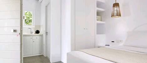 A modern bedroom with a large bed, a wardrobe, and a bathroom visible in the background.