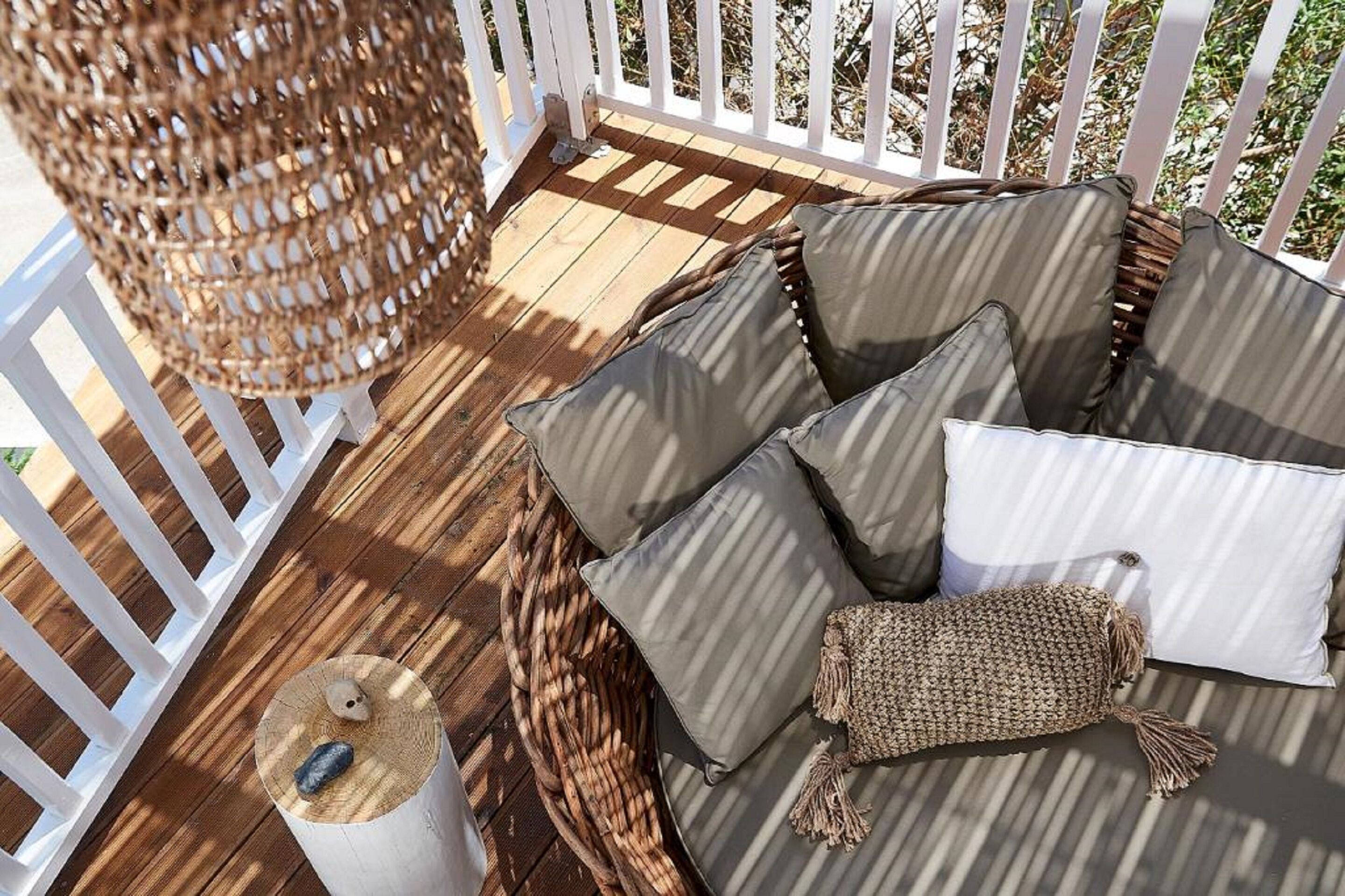 A wicker sofa with cushions on a wooden deck, a woven basket, and a white post.