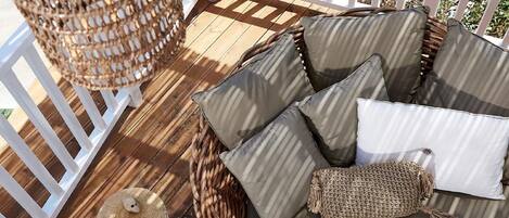 A wicker sofa with cushions on a wooden deck, a woven basket, and a white post.