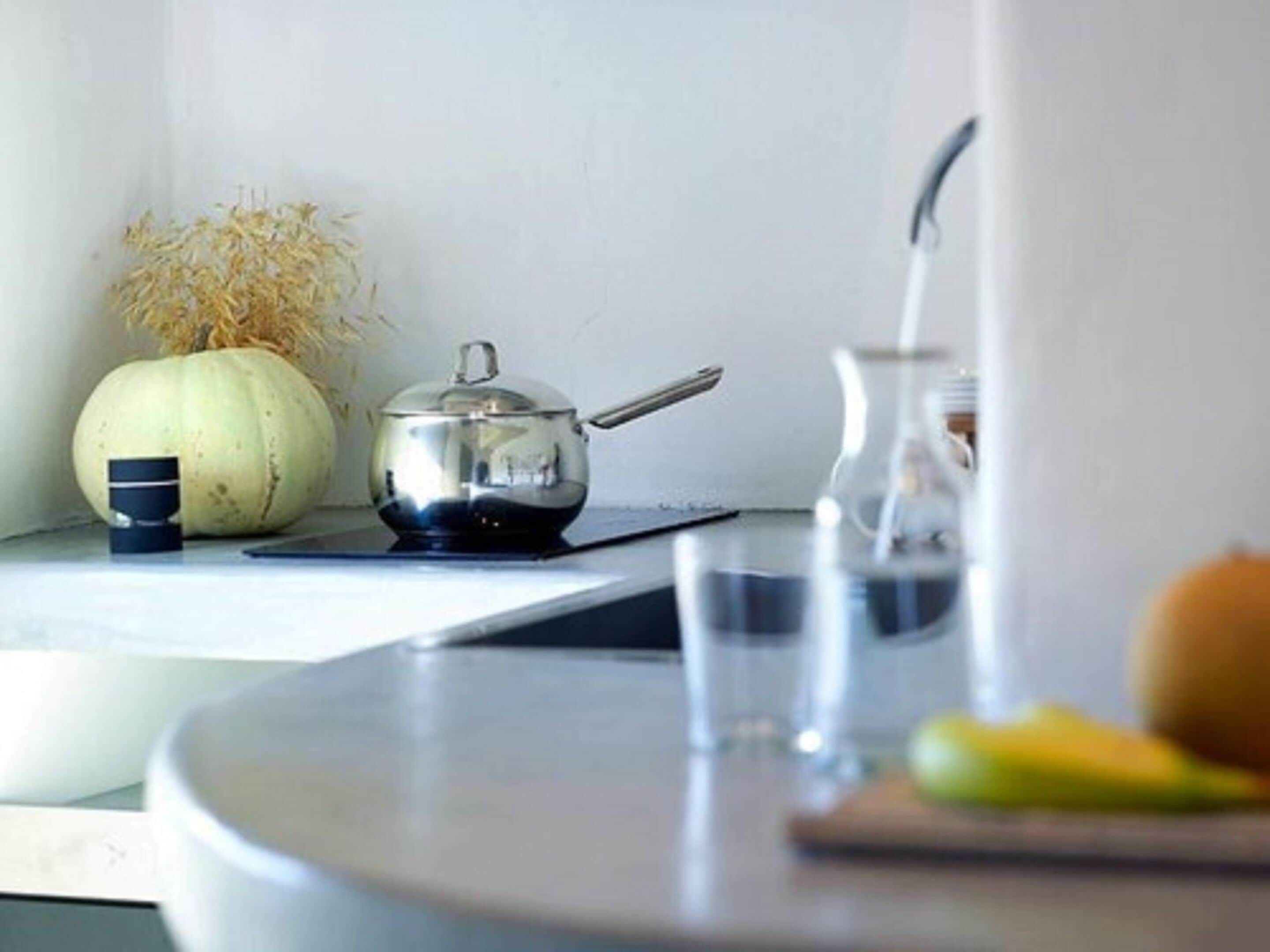 A kitchen counter with a kettle, a pumpkin, a glass, and a cutting board with vegetables.