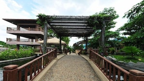 A bridge with a wooden railing, leading to a building with multiple balconies and a covered walkway. - Chart Thip Resort (Sung Noen)