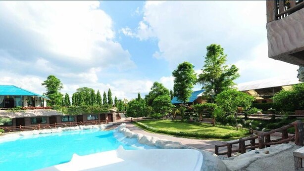A swimming pool with a surrounding deck, trees, and a building with a blue roof. - Chart Thip Resort (Sung Noen)