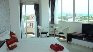 A hotel room with a bed, a TV, a desk, and a balcony with a view of the city. - Grand Residence Jomtien (Pattaya)