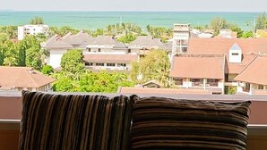 A balcony with a striped cushion, overlooking a residential area with houses and a view of the ocean. - Grand Residence Jomtien (Pattaya)