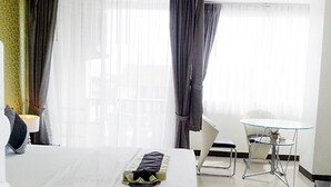 A hotel room with a bed, a small round table, a chair, and a window with curtains. - Grand Residence Jomtien (Pattaya)
