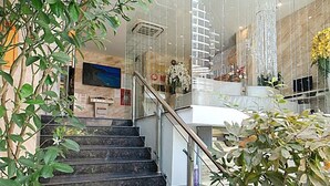 A modern hotel lobby with a glass staircase, marble flooring, and a chandelier. - New Sun Hotel (Nha Trang)