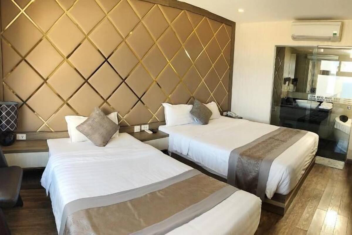 Une chambre d’hôtel avec deux lits, un bureau, une chaise, un miroir et un appareil de climatisation.