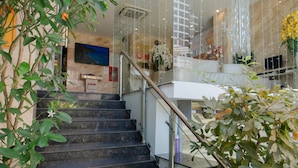 A modern interior with a glass staircase, a chandelier, and indoor plants. - New Sun Hotel (Nha Trang)