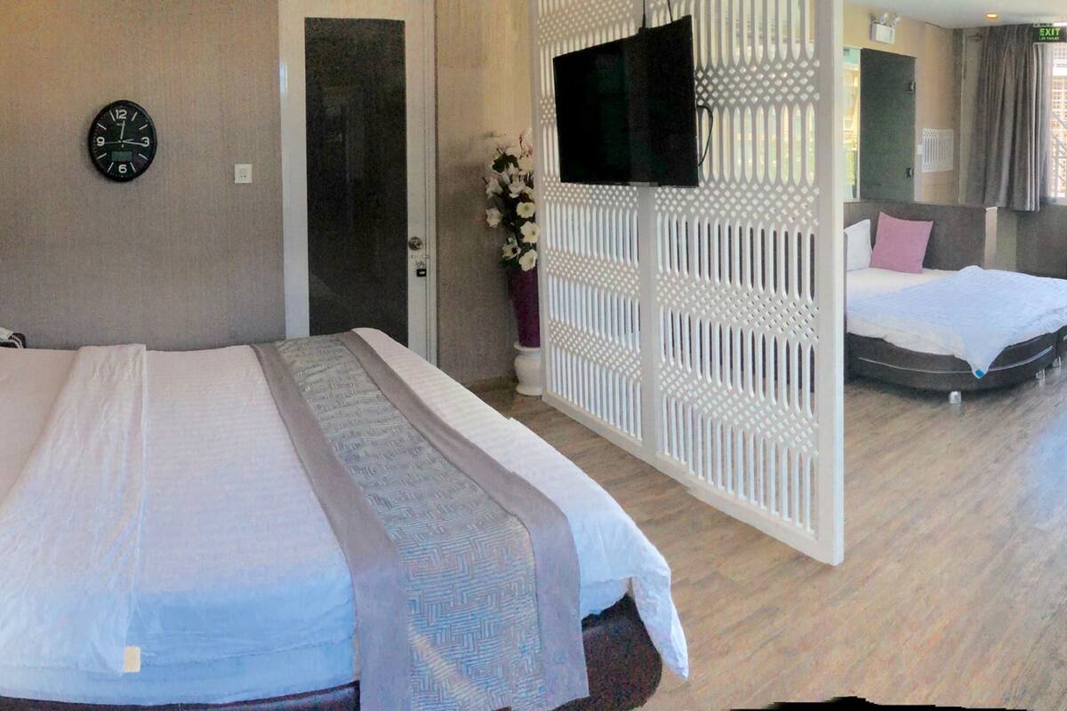 Une chambre d’hôtel avec un grand lit, un deuxième lit, une télévision, une horloge et une vue sur la ville.