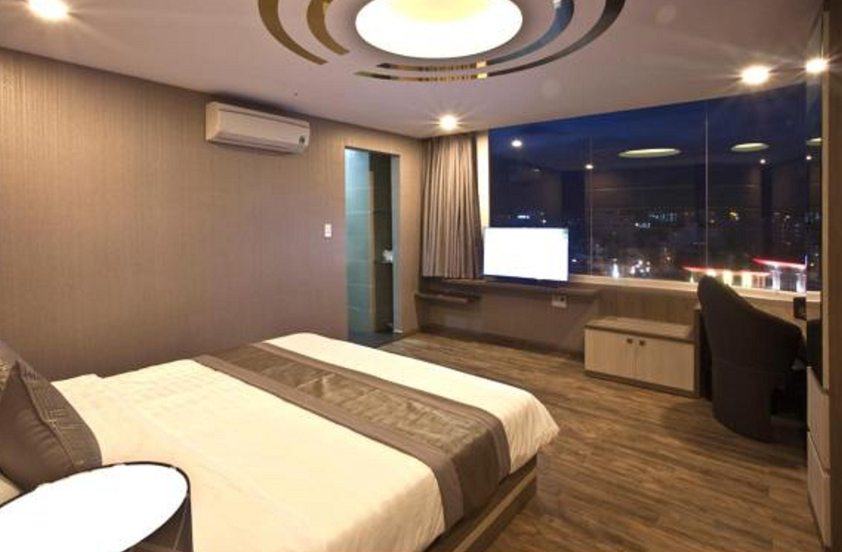 Habitación de hotel con una cama grande, un escritorio, una silla y una ventana con vistas a la ciudad.