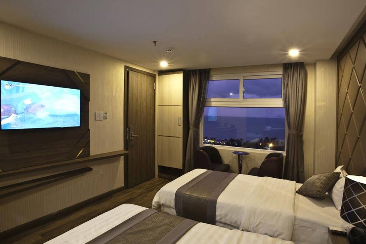 Une chambre d’hôtel avec un lit, un téléviseur fixé au mur, une fenêtre avec des rideaux et une vue sur la ville la nuit.