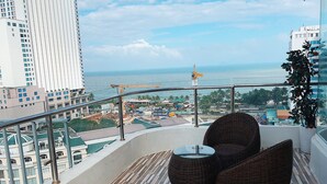 A balcony with wicker furniture, a view of the sea, and high-rise buildings. - New Sun Hotel (Nha Trang)