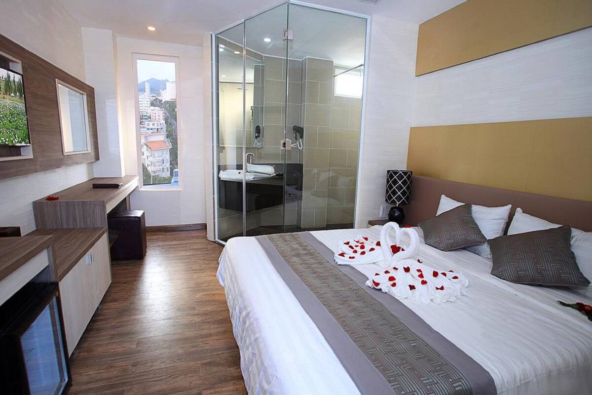 Une chambre d’hôtel moderne dotée d’un grand lit, d’une douche à parois de verre, d’une petite salle de bain et offrant une vue sur la ville.
