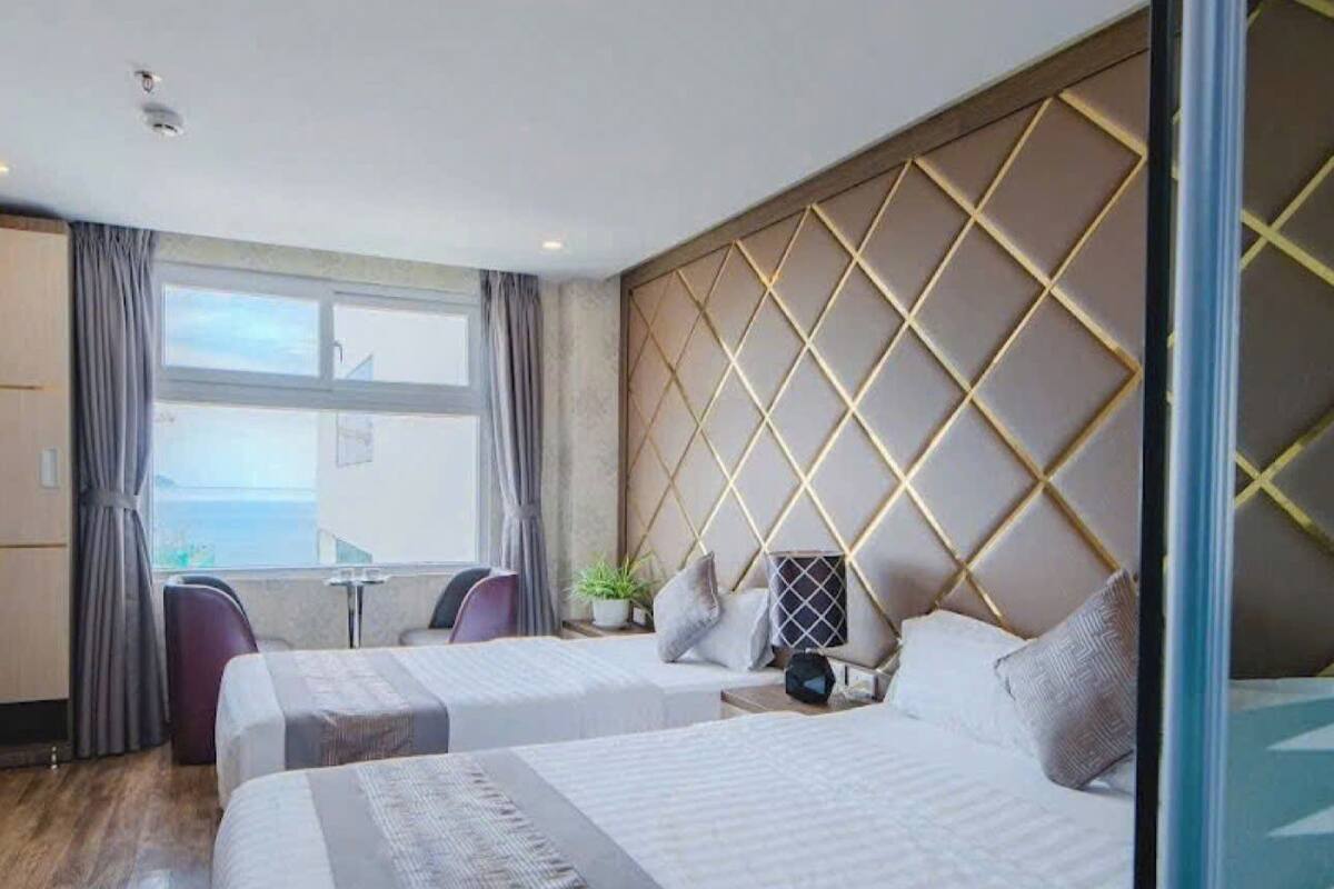 Une chambre d’hôtel avec un grand lit, un coin salon avec un canapé et des fauteuils, une petite table et une vue sur la mer.