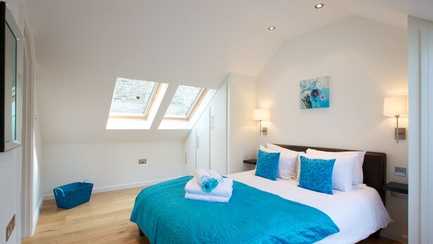 Une chambre avec un grand lit, des fenêtres de toit, un mur d’accent bleu et un tableau.