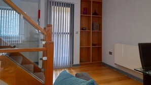 Un salon doté d’un plancher en bois, d’une porte vitrée donnant sur un balcon et d’une bibliothèque intégrée en bois.