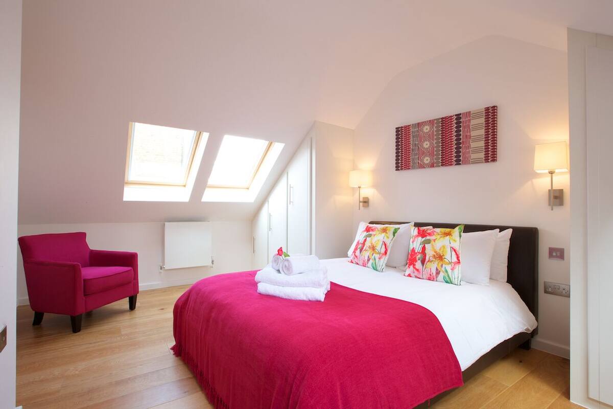 A bedroom with a red bedspread, a pink chair, and two skylights.