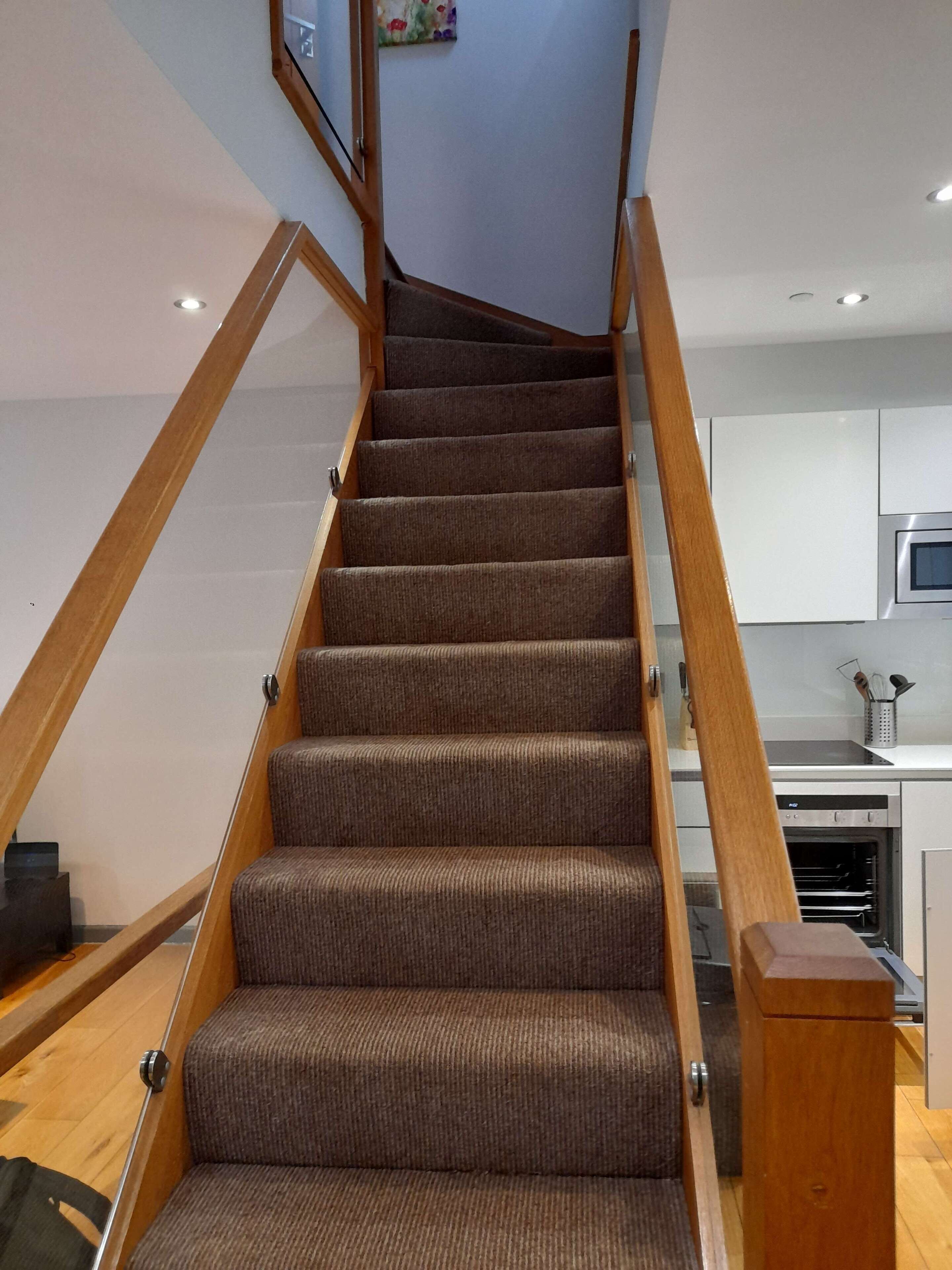 A staircase with wooden handrails and carpeted steps leading to a kitchen area with white cabinets and a microwave.