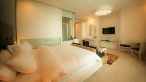 Une chambre d’hôtel moderne dotée d’un grand lit, d’un coin salon avec un téléviseur et d’une salle de bain avec un miroir et un lavabo.