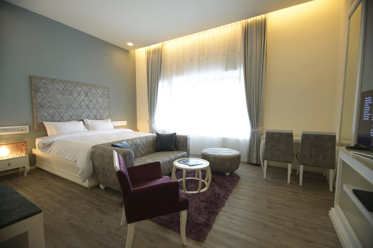 A modern hotel room with a large bed, a seating area with a round table, and a television on a stand.