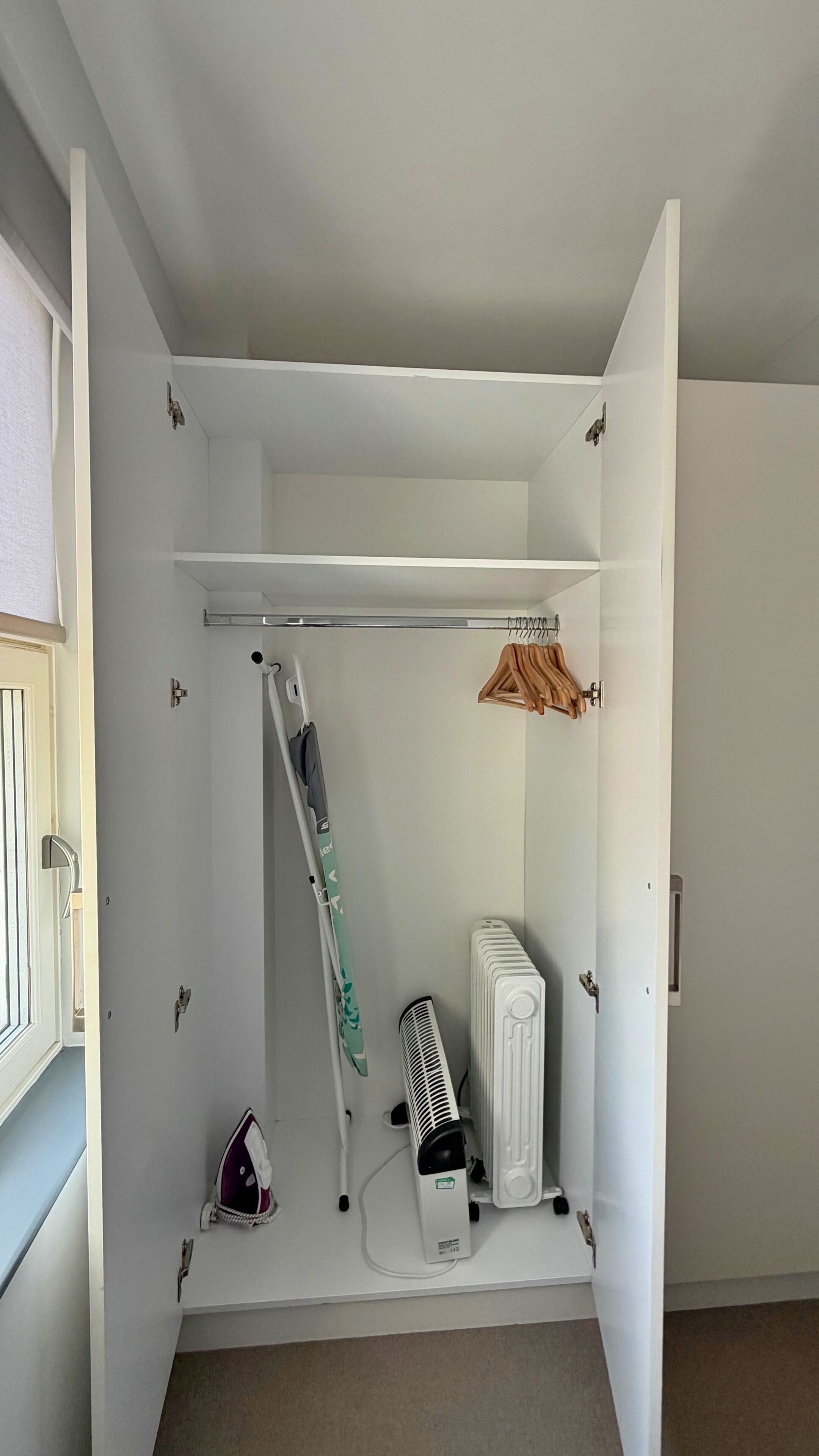 A room with a white radiator, a standing fan, a green towel, and a wooden hanger rack.