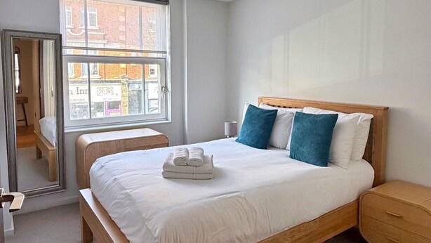 A modern bedroom with a wooden bed, a nightstand, and a window with a view of buildings.