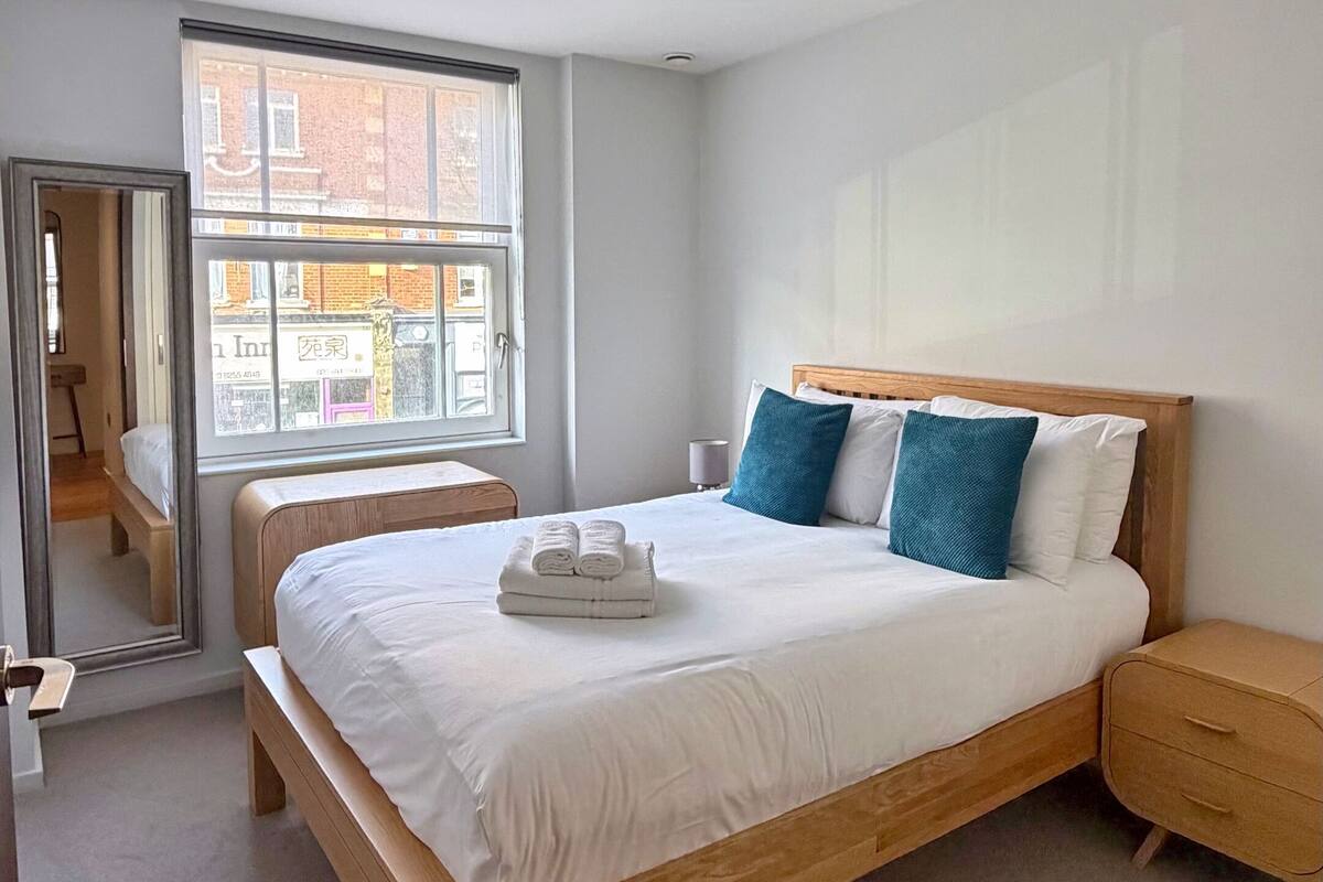 A modern bedroom with a wooden bed, a nightstand, and a window with a view of buildings.