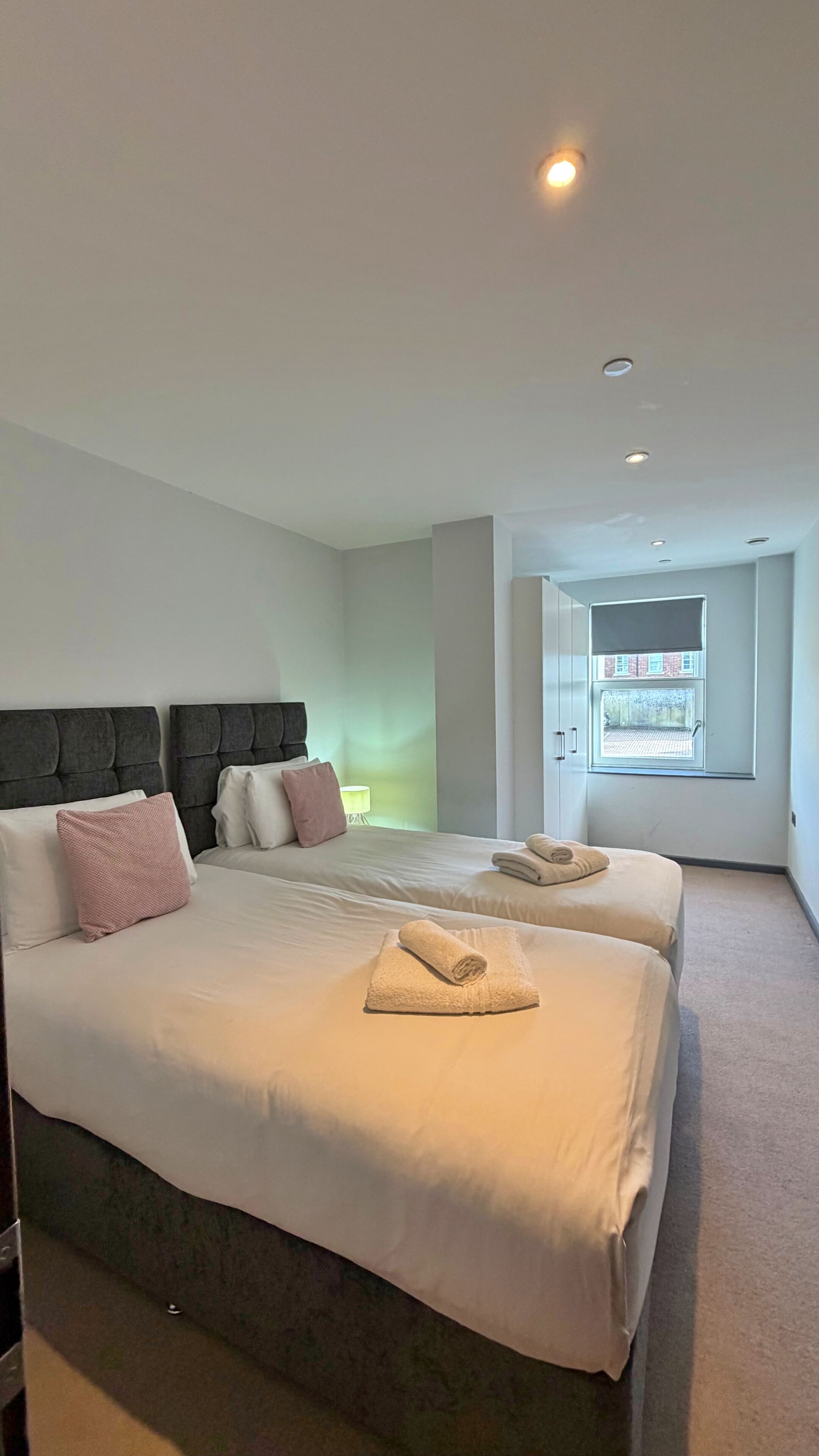 A modern hotel room with two beds, a large window, and a view of the outside.