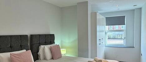 A modern hotel room with two beds, a large window, and a view of the outside.