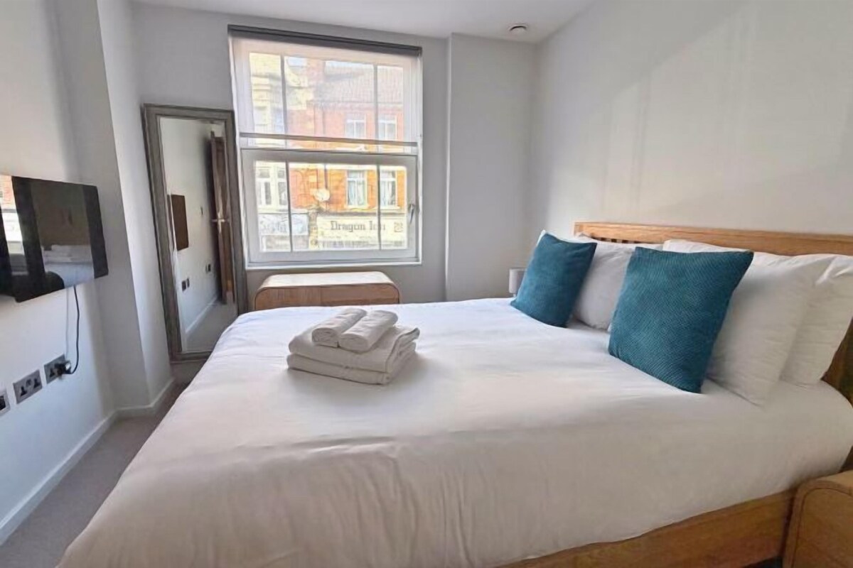 Quarto de hotel com uma cama grande, televisão na parede e janela com vista para edifícios.