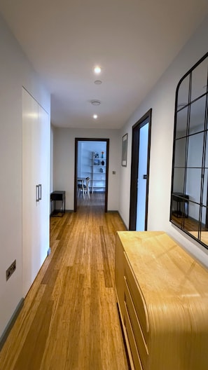 Um corredor com piso de madeira, uma cama, um guarda-roupa e uma janela com moldura de metal.