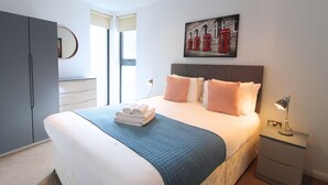 A neatly made bed with a blue quilt, a bedside lamp, and a painting of red telephone booths on the wall. - London Bridge – Tooley St by Viridian Apartments (London)