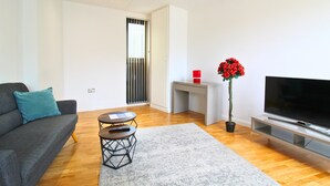 A modern living room with a grey sofa, a small round table, a flat-screen TV, and a potted plant. - London Bridge – Tooley St by Viridian Apartments (London)