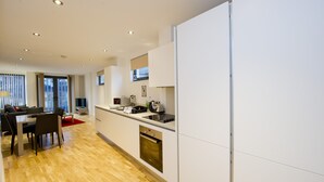 A modern kitchen with white cabinets, a built-in oven, and a dining area with a table and chairs. - London Bridge – Tooley St by Viridian Apartments (London)