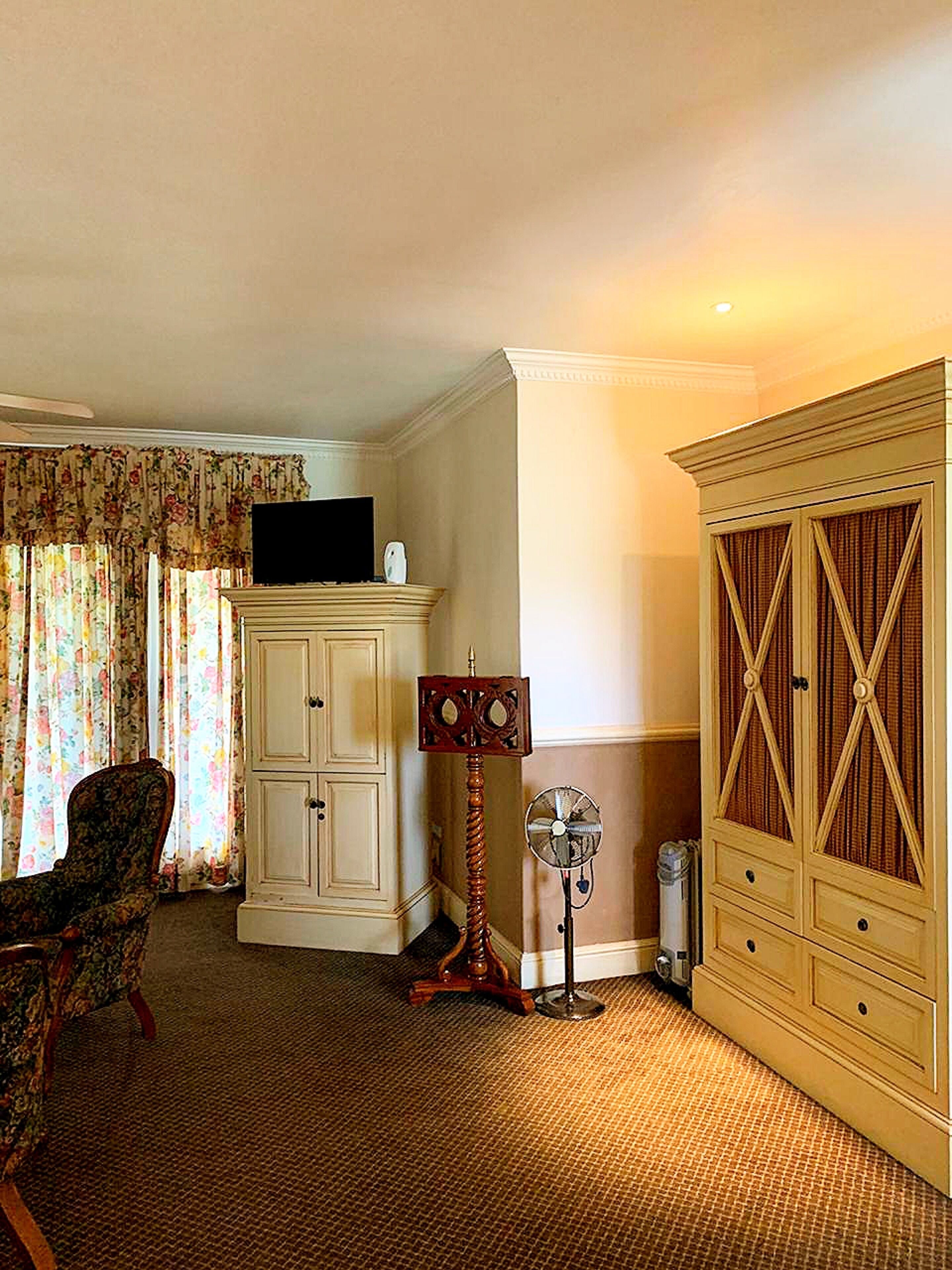 Een kamer met een televisie op een kast, een ventilator en een stoel.