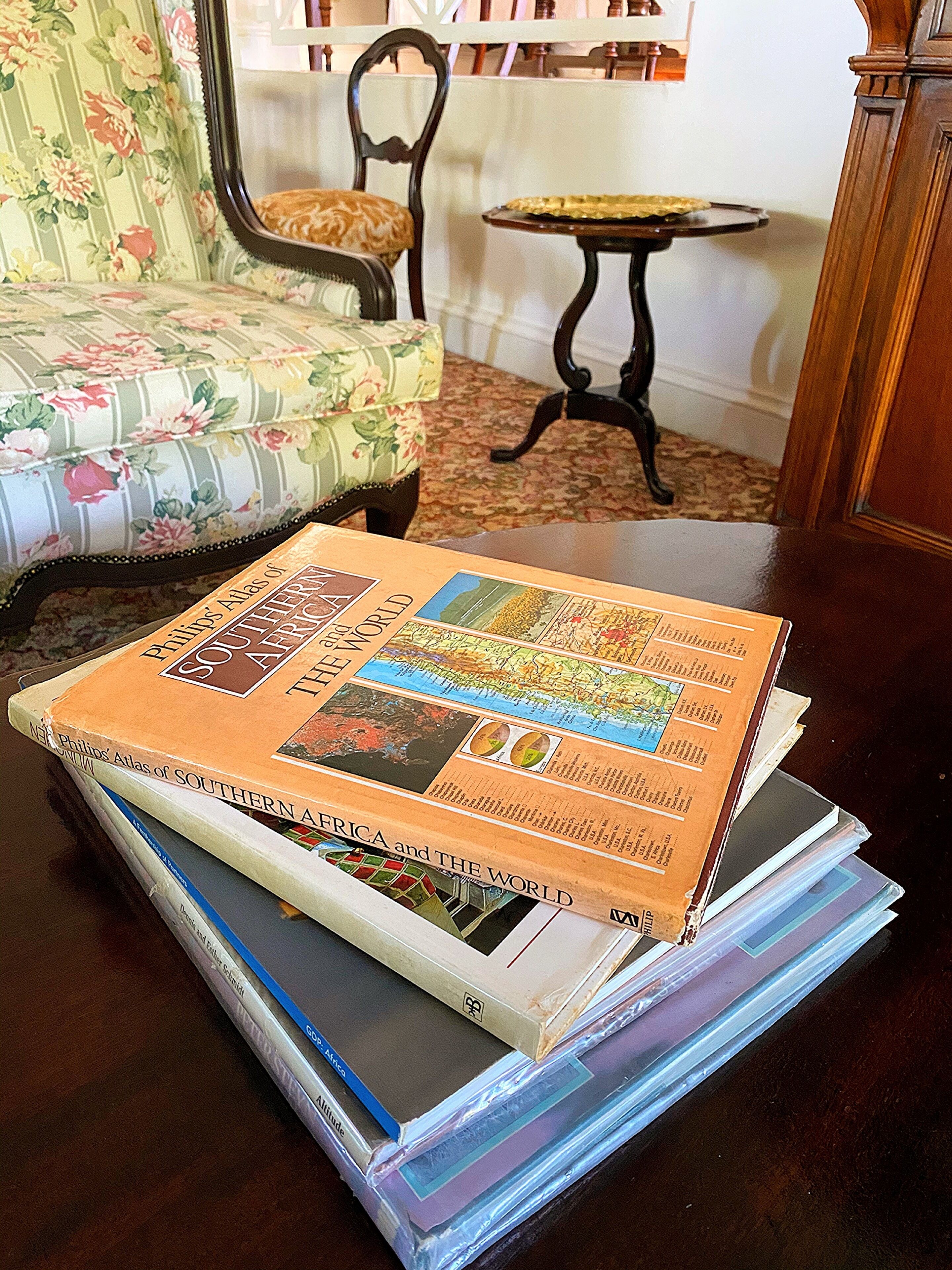 A stack of books titled 'Phillips' Atlas of Southern Africa and the World' on a wooden table.