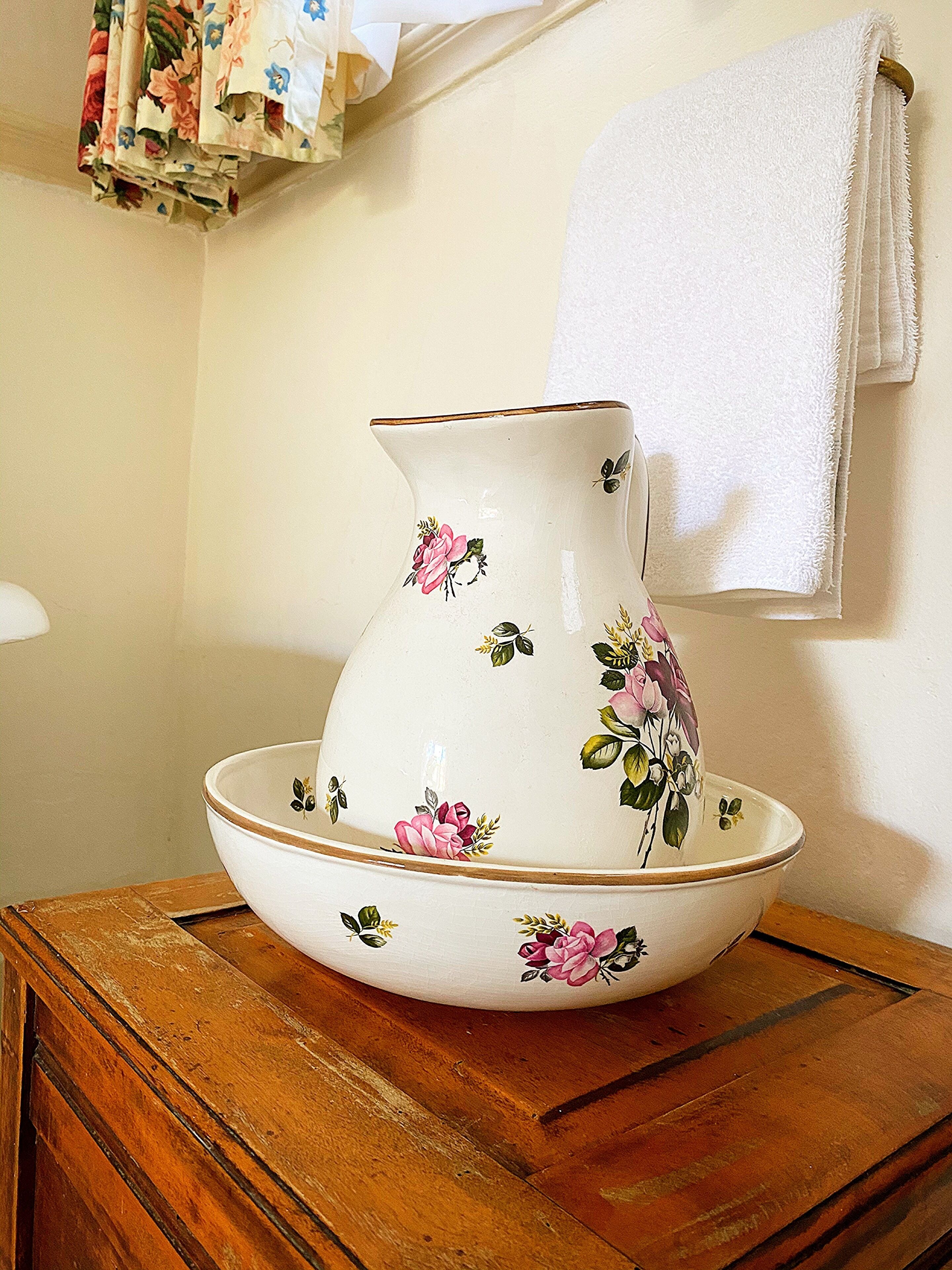Een witte keramieken pitcher met bloemmotieven op een houten tafel.