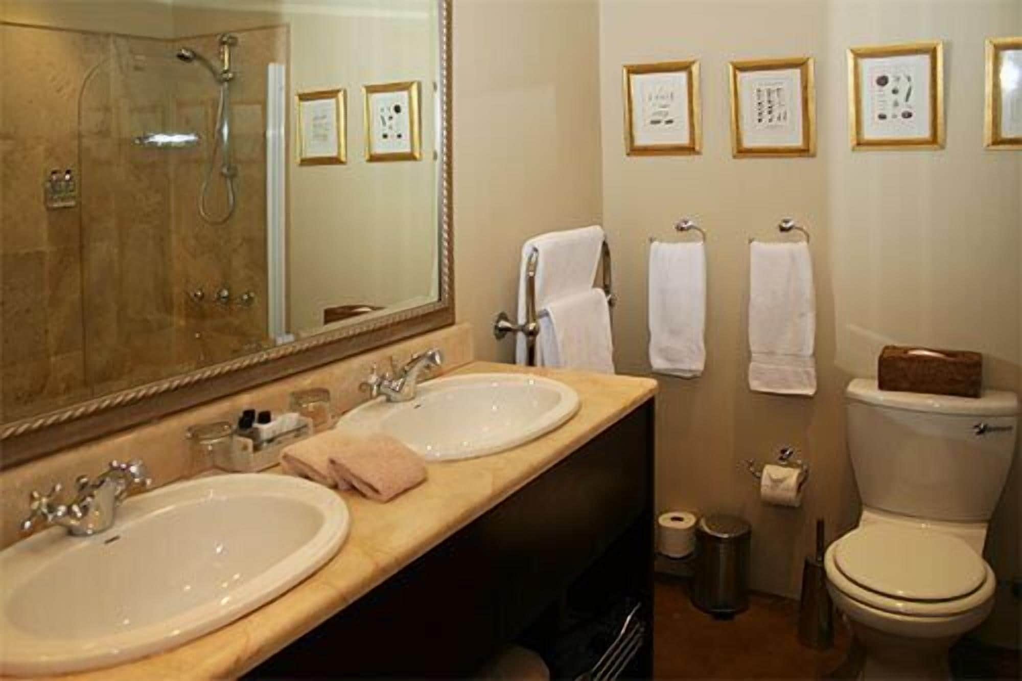 A bathroom with two sinks, a shower, and a toilet. There are framed certificates on the wall.