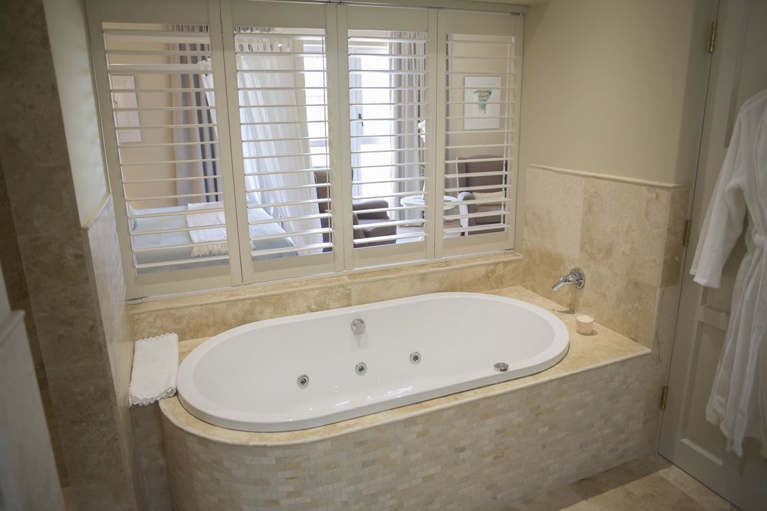 Ein Badezimmer mit freistehender Badewanne, einem Fenster mit Jalousien und einem Handtuchhalter.