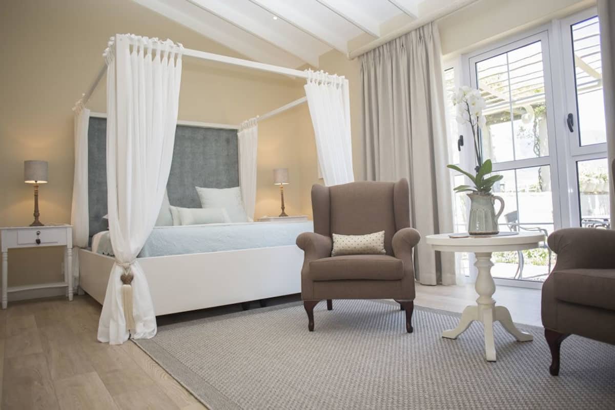 Een slaapkamer met een hemelbed, twee nachtkastjes, een stoel, een tafel en een vaas met bloemen.