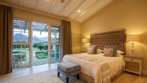 A bedroom with a large bed, two bedside lamps, a nightstand, a window with curtains, and a view of the outdoors.