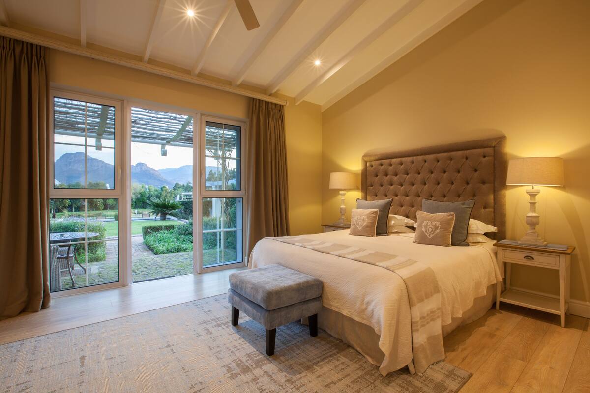 Een slaapkamer met een groot bed, twee bedlampen, een nachtkastje, een raam met gordijnen en uitzicht op de omgeving.